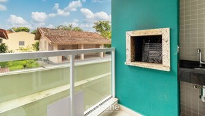 Un balcón con vista a una casa vecina y una pared de azulejos con una ventana pequeña.