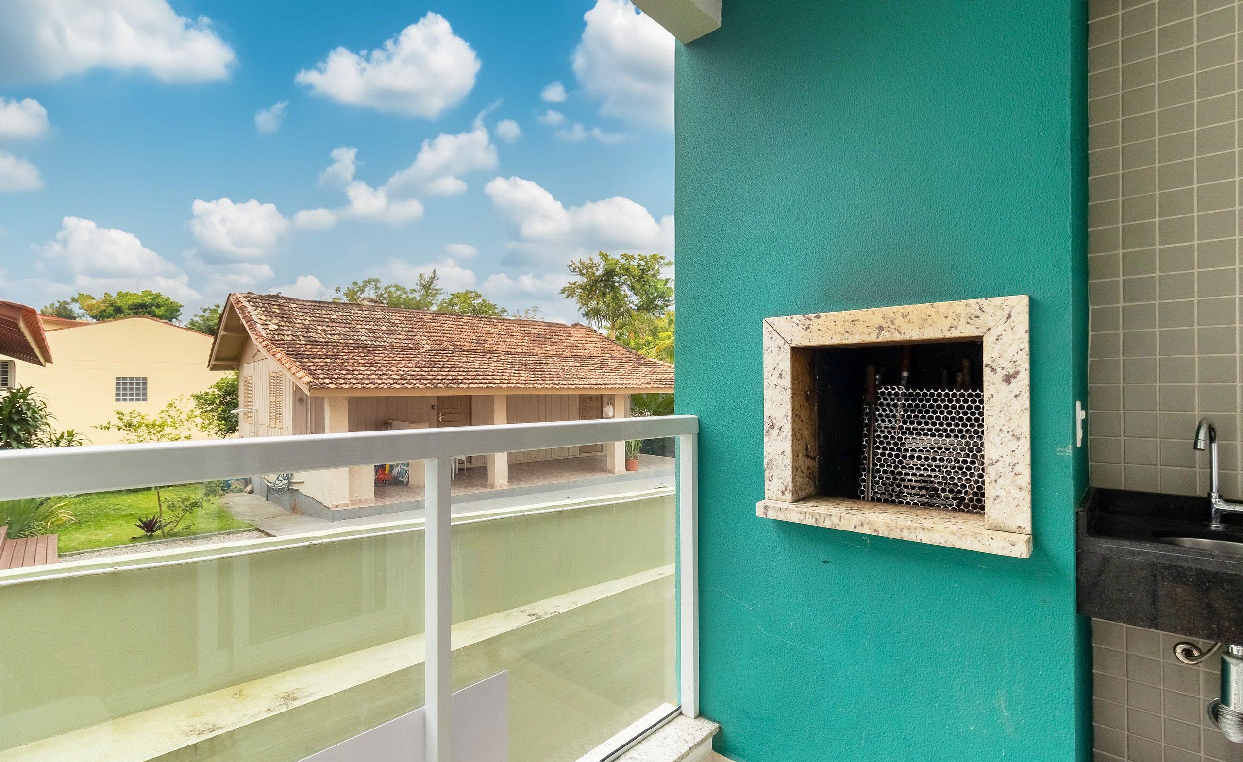 A balcony with a view of a neighboring house and a tiled wall with a small window.