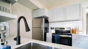 A modern kitchen with stainless steel appliances, a black faucet, and white cabinetry.