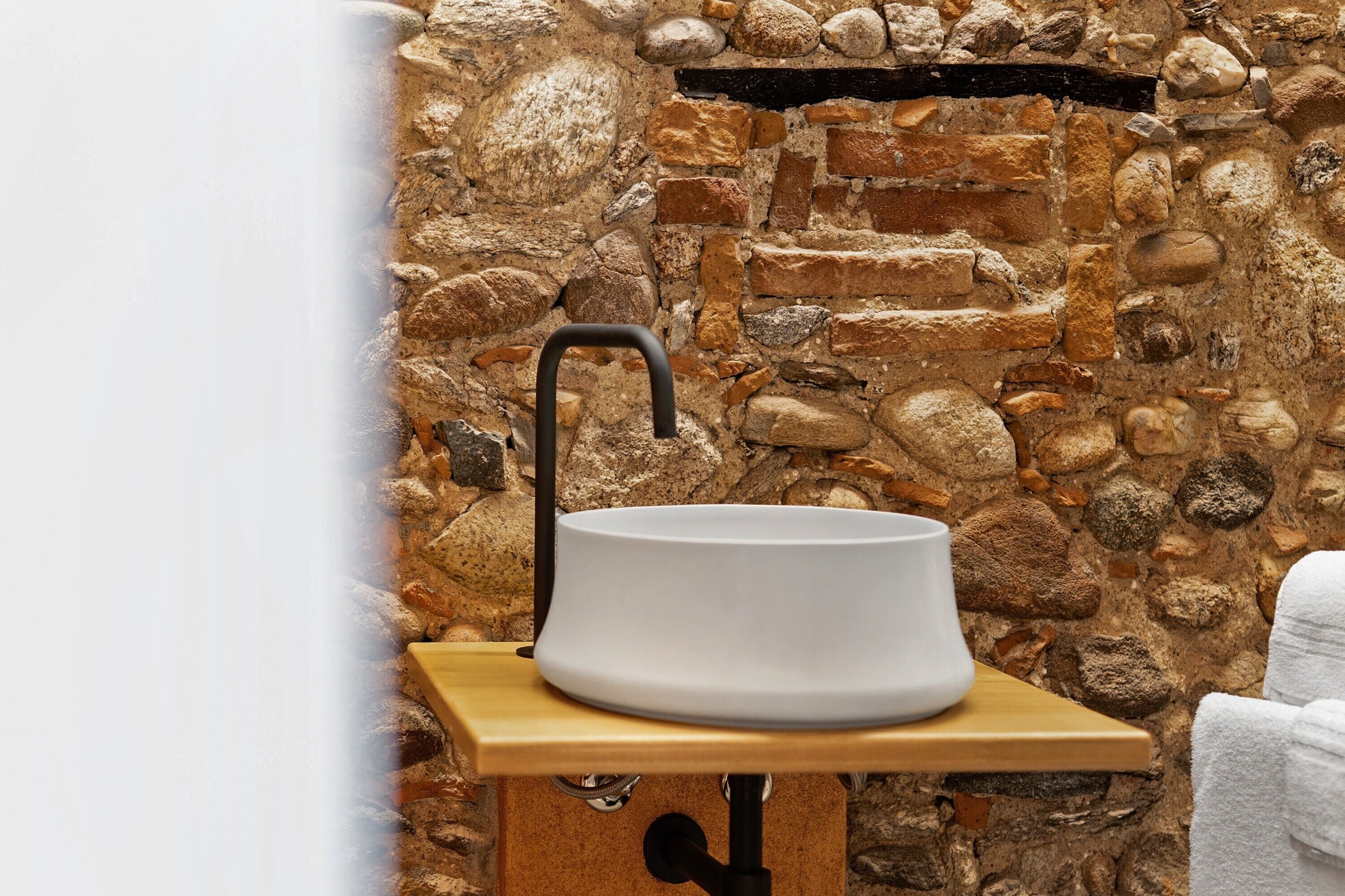 A bathroom with a stone wall, a white sink, and a wooden shelf.