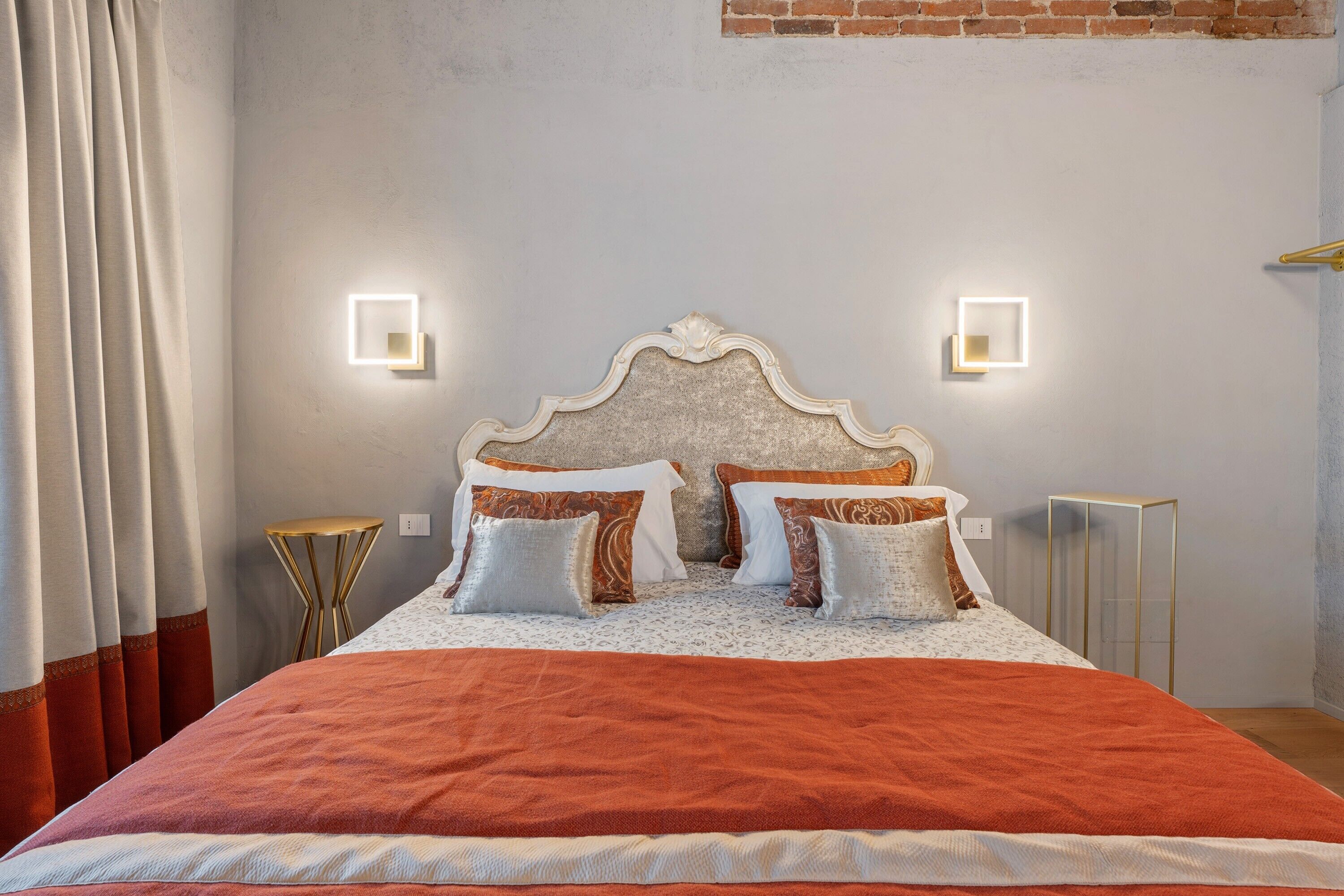 A bed with a headboard, two bedside tables, a curtain, and a wall with a brick pattern.