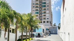 Un edifici residencial de diversos pisos amb balcons, una entrada tancada amb reixa i palmeres al primer terme.