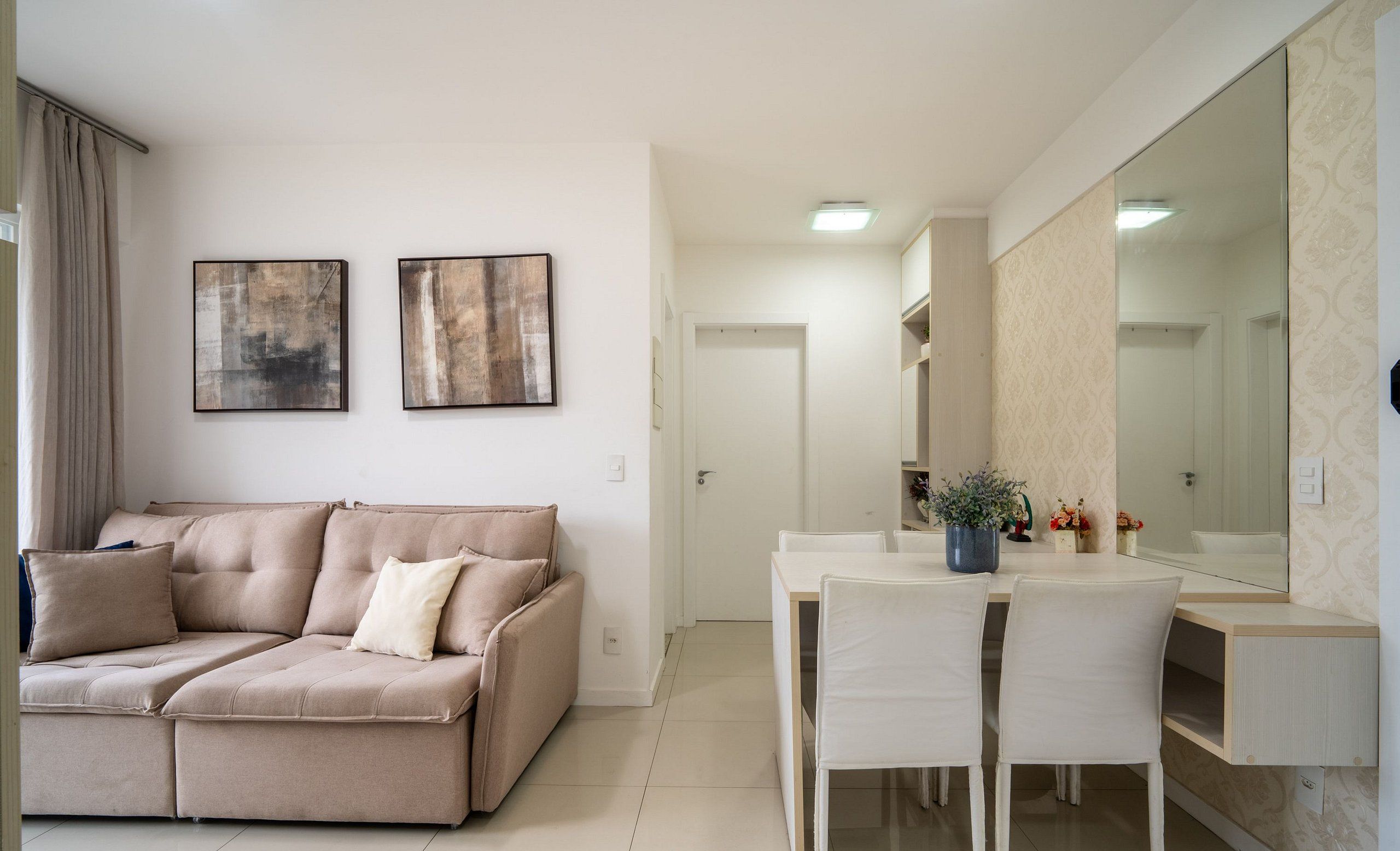 Una sala moderna con un sofá seccional beige, una mesa de comedor con sillas y un espejo grande.