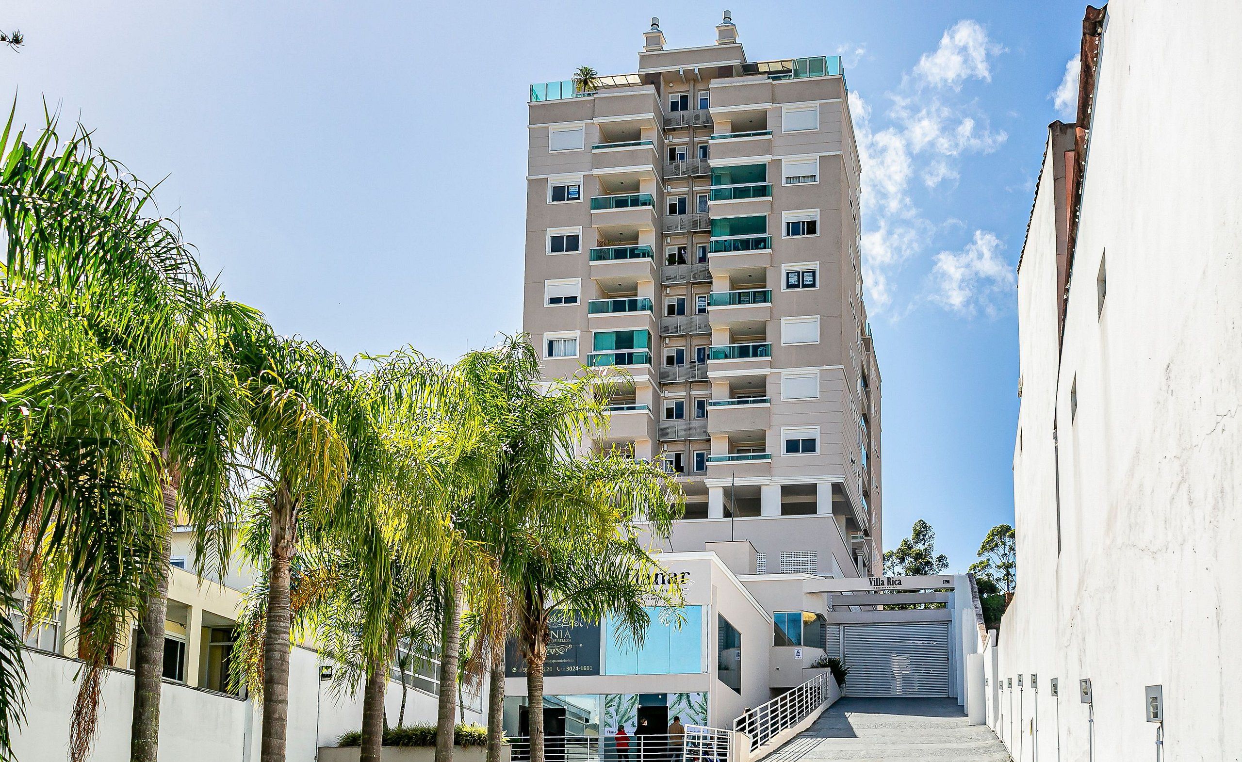 Un edificio residencial de varios pisos con balcones, una entrada con reja y palmeras en primer plano.