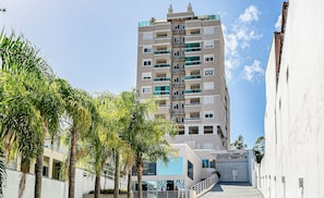A multi-story residential building with balconies, a gated entrance, and palm trees in the foreground. - Beautiful and Comfortable apt Front of Ufsc Rvr0506 (Florianópolis)
