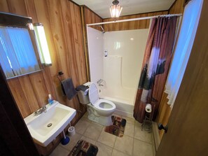 Ein Badezimmer mit Holzvertäfelung, einem weißen Waschbecken, einer Toilette und einer Duschkabine.