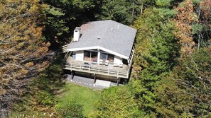 Ein Haus mit einem geneigten Dach und einem Balkon mit Gartenmöbeln, umgeben von dichtem Wald.