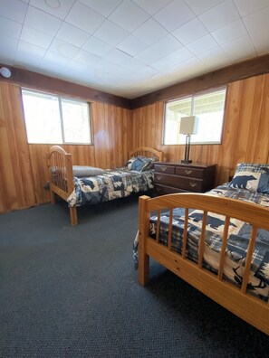 A room with two wooden beds, a dresser, and a chair.