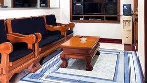 A living room with a sofa, chairs, a coffee table, a large mirror, a window with shelves, and a water dispenser.