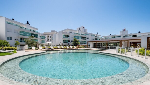 Un hotel moderno con piscina central, mobiliario exterior y un cielo azul despejado.