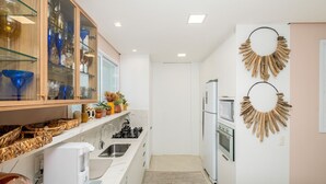 Una cocina moderna con armarios blancos, horno empotrado y cafetera. Hay objetos decorativos en los estantes y una alfombra pequeña en el suelo.