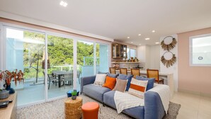 Una sala de estar moderna con un sofá azul, un comedor y una cocina con vista a zonas verdes.