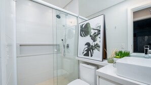 Un baño moderno con cabina de ducha de vidrio, lavamanos blanco y planta en marco.