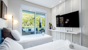 Habitación de hotel moderna con dos camas, televisión y balcón con vistas a la vegetación.