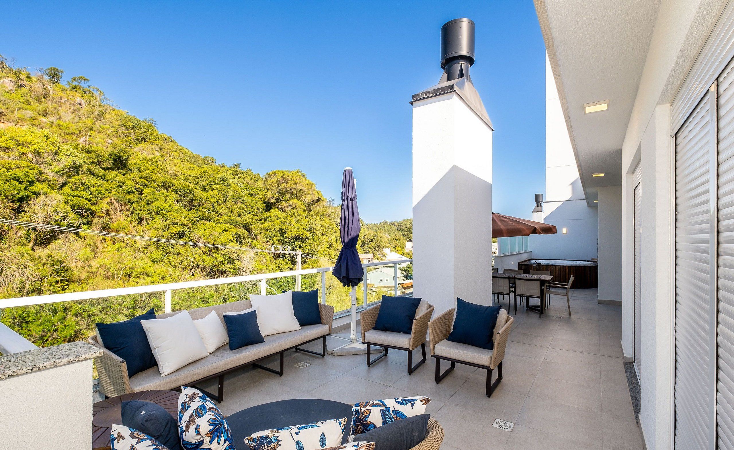 Un balcón con mobiliario exterior, una chimenea y vistas a una ladera verde y exuberante.