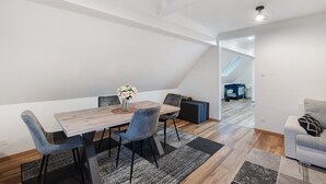 Un comedor con mesa de madera, sillas azules, un jarrón con flores y vistas a un espacio tipo loft.