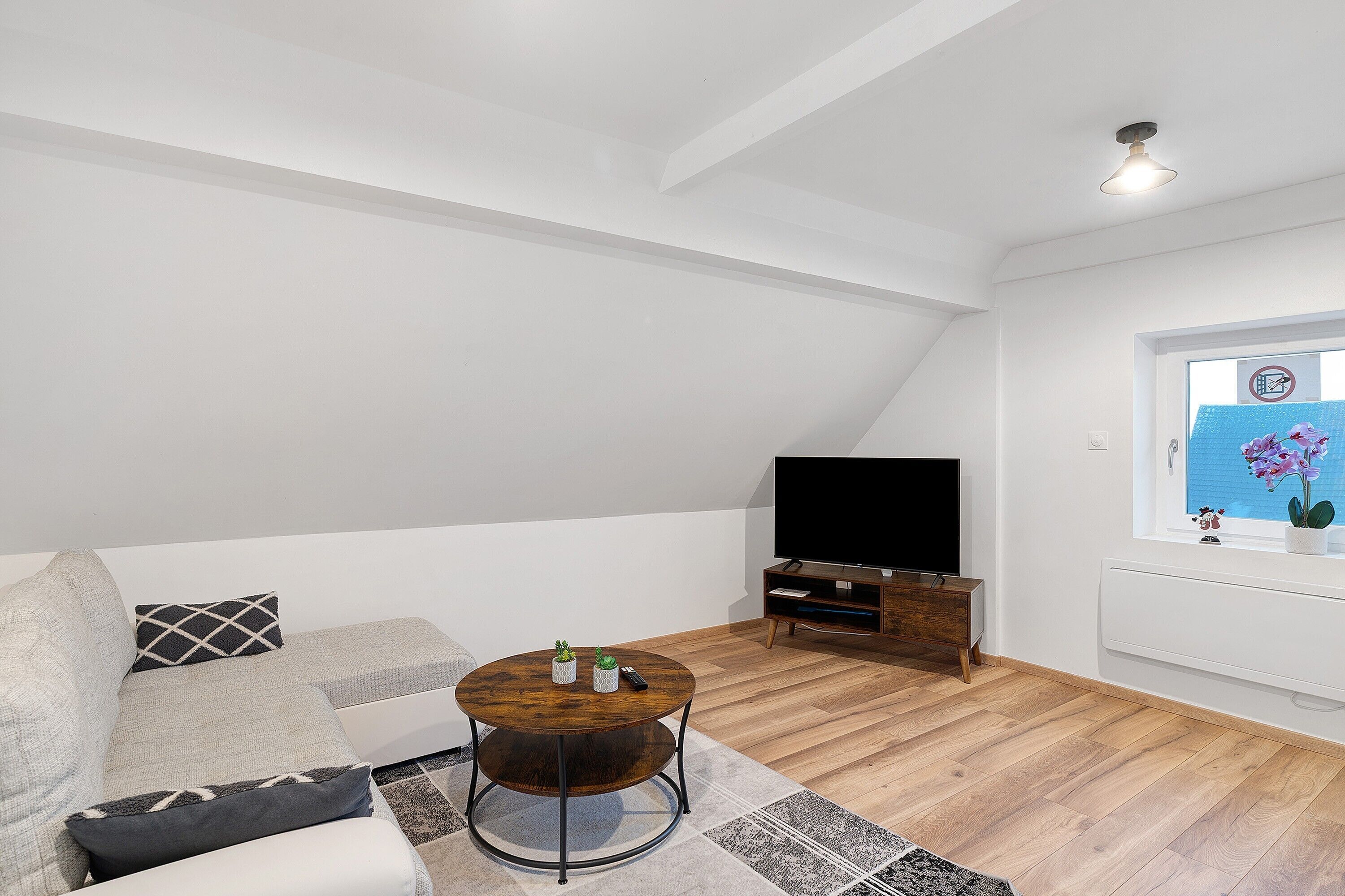 A modern living room with a sofa, round coffee table, TV, and wooden flooring.