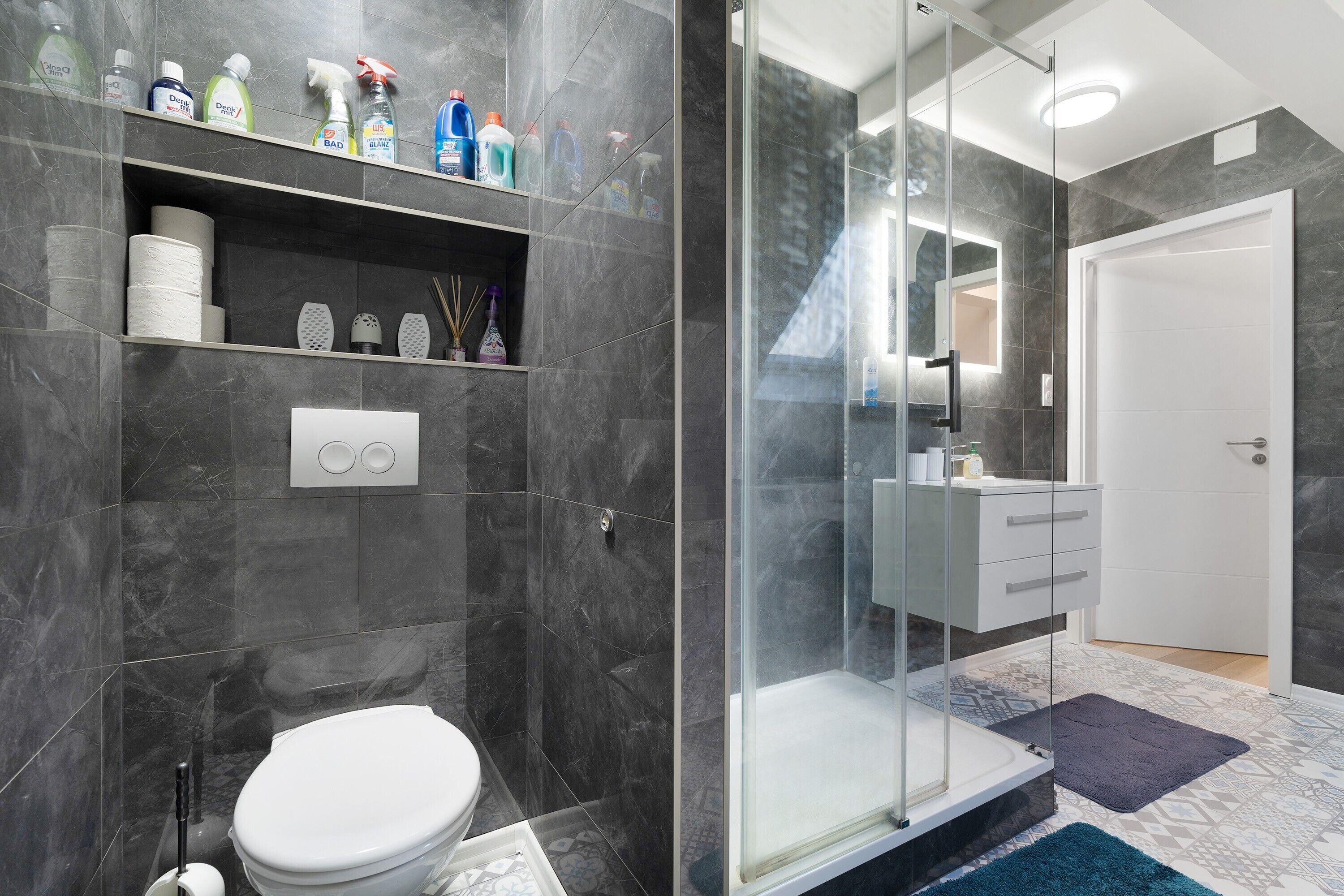 Un baño moderno con inodoro, ducha y zona de ducha con mampara de vidrio.