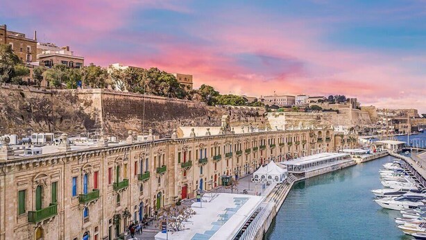 Un paseo marítimo con edificios históricos, un puerto deportivo y vistas al mar.