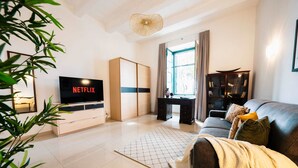 Una sala de estar moderna con un televisor de pantalla plana, un sofá, una estantería y un ventanal grande.