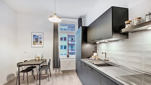 Een moderne keuken met een eetgedeelte, met een raam met uitzicht op gebouwen, een hanglamp en een ingebouwde oven.