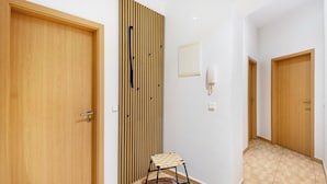 Een hal met houten deuren, een wand van verticale houten latten, een klein krukje en een wandlamp.