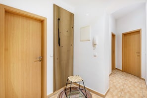 Un pasillo con puertas de madera, un revestimiento de listones verticales de madera, un taburete pequeño y un aplique de pared.
