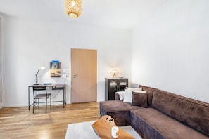 A modern living room with a wooden floor, a brown sofa, a desk with a chair, and a door.