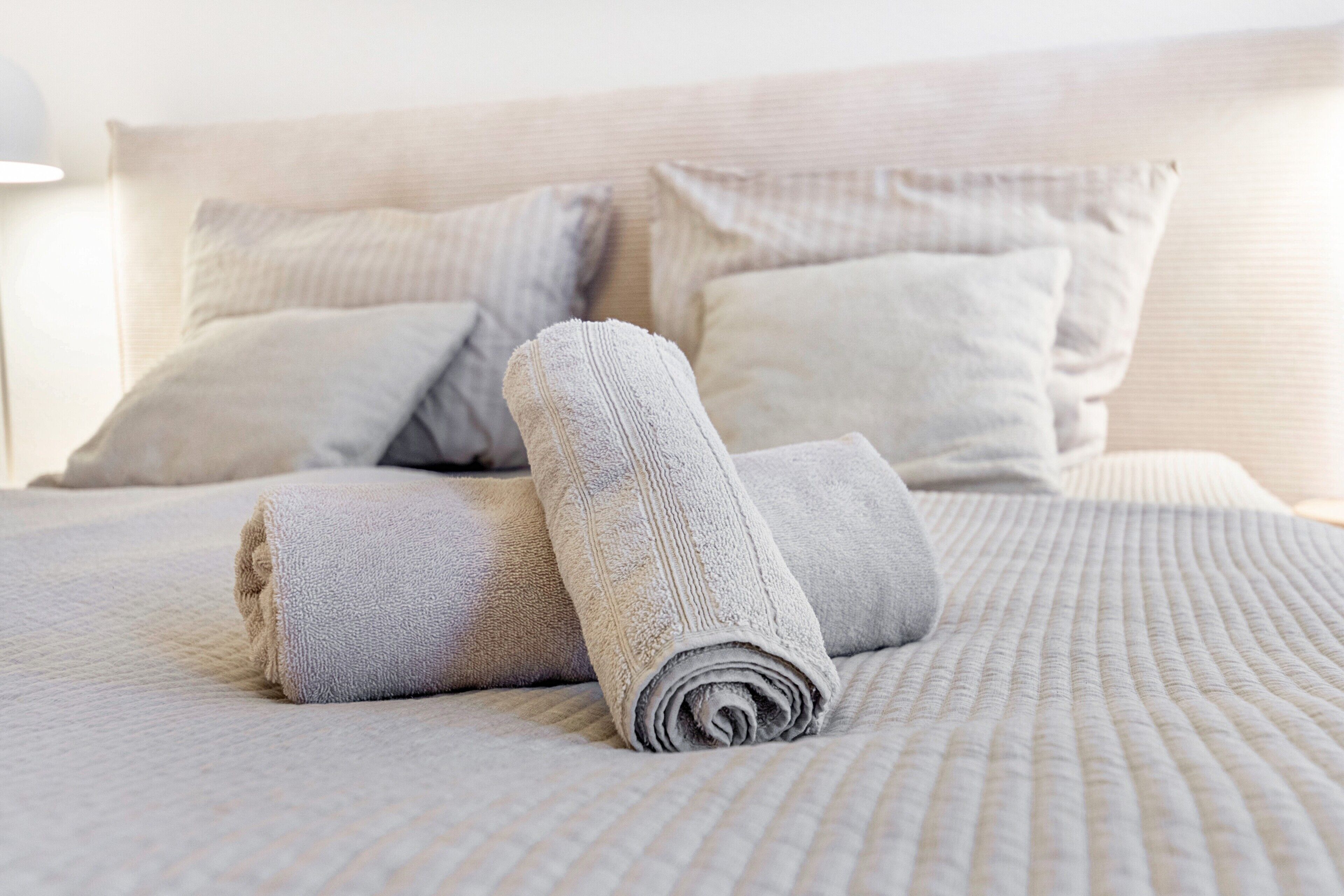 Een opgemaakt bed met opgerolde handdoeken en kussens.