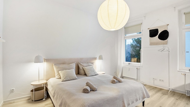 Een slaapkamer met een groot bed, nachtlampjes, een hanglamp en uitzicht op het omliggende landschap.