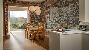 Un'ampia sala da pranzo con parete in pietra, sedie in legno e una grande finestra con vista su un paesaggio pittoresco.