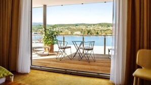 A balcony with a wooden floor, two chairs, a table, and a potted plant. - Seehotel Süd (Velden am Wörther See)