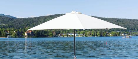 Terraza junto al lago con dos tumbonas y una sombrilla blanca.