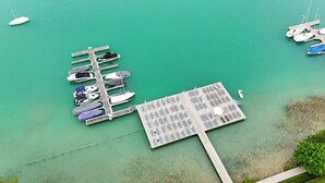 An aerial view of a marina with boats docked at a pier and a separate area with sun loungers and umbrellas. - Seehotel Süd (Velden am Wörther See)