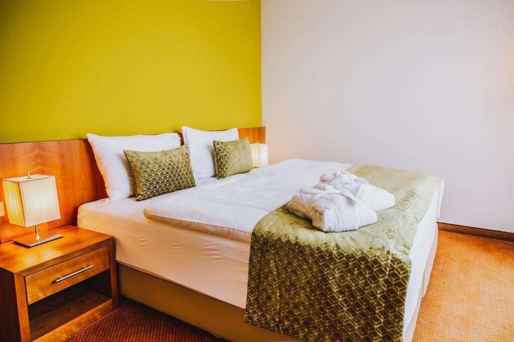 A hotel room with a bed, a nightstand with a lamp, and a green wall.