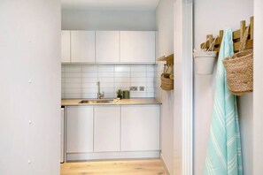 A kitchen with white cabinets, a sink, and a countertop. There are baskets and a towel hanging on the wall.