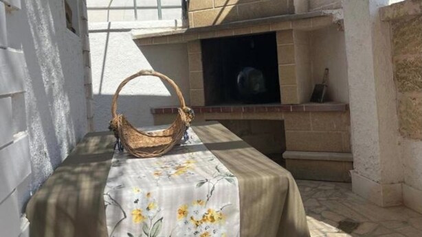 An outdoor patio with a table covered in a floral tablecloth, a wicker basket, and a stone-tiled floor. - Three-room cottage Luis (Torre Suda)