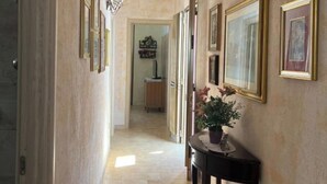 A hallway with framed pictures on the walls, a wooden table with a plant, and a door leading to another room. - Three-room cottage Luis (Torre Suda)
