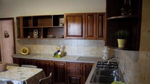 A kitchen with wooden cabinets, a sink, a stove, and a table with chairs. - Three-room cottage Luis (Torre Suda)