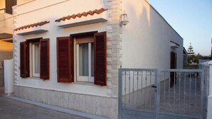 A building with a white facade, red shutters, and a metal gate. - Three-room cottage Luis (Torre Suda)