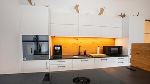 Una cocina moderna con armarios blancos, un protector contra salpicaduras de madera, una máquina de café, un microondas y una placa de cocción por inducción negra.