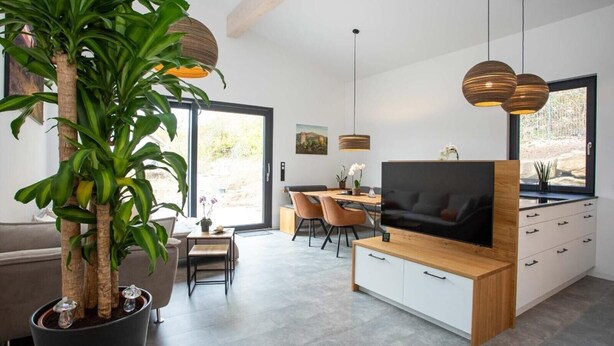 Una sala de estar moderna con un televisor grande, armarios de madera, una zona de comedor y una planta en maceta.