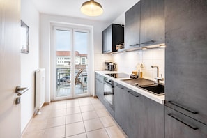 Une cuisine moderne dotée d’une grande fenêtre, offrant une vue sur les immeubles, et d’une porte coulissante donnant sur un espace extérieur.