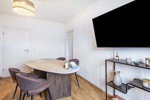 Une pièce moderne avec une table à manger ronde, des chaises, un téléviseur fixé au mur et une étagère contenant divers objets.