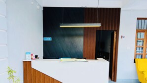 A reception desk with a wooden finish and a white counter. There is a sign on the wall and a potted plant to the left. - Hotel Insta 18 (Siliguri)