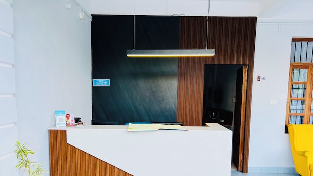 A reception desk with a wooden finish and a white counter. There is a sign on the wall and a potted plant to the left. - Hotel Insta 18 (Siliguri)