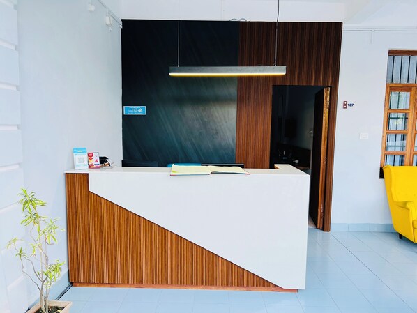 A reception desk with a wooden finish and a white counter. There is a sign on the wall and a potted plant to the left. - Hotel Insta 18 (Siliguri)