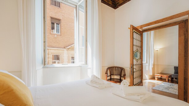 A hotel room with a large bed, a wooden chair, a small table, and a mirror. - Rental in Rome Frattina Atmosphere Apartment (Rome)