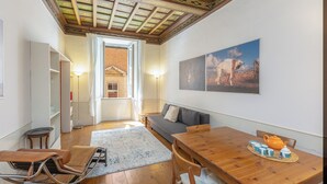 A cozy room with a wooden dining table, a sofa, and a view of a countryside landscape through a window. - Rental in Rome Frattina Atmosphere Apartment (Rome)