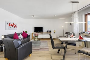 Ett modernt vardagsrum med en soffa, ett matbord, stolar, en platt-TV och ett stort fönster.